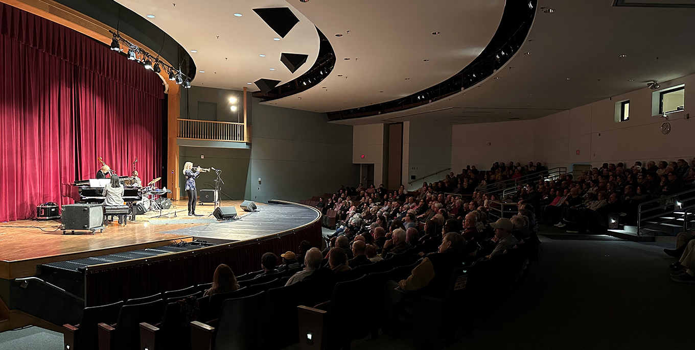 Woman playing trumpet on stage in JBK Theatre with audience watching