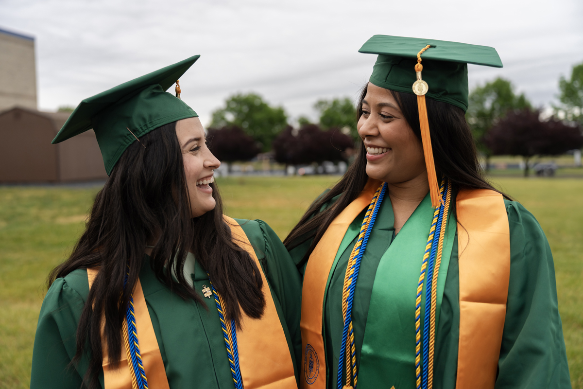 A graduate smiling with friends while holding their diploma cover