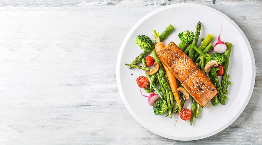 White plate with salmon on bed of vegetables