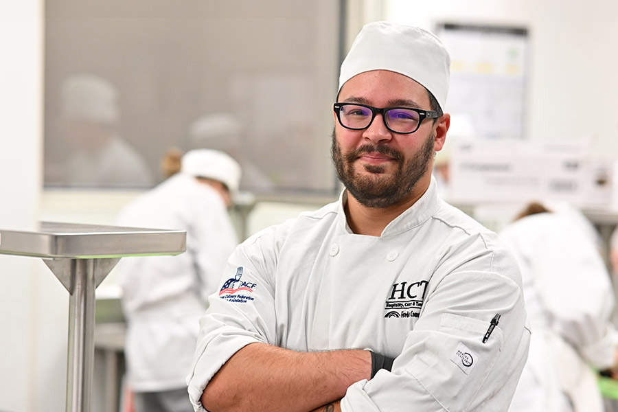 HCTI culinary student in chef whites standing with arms crossed in a kitchen classroom