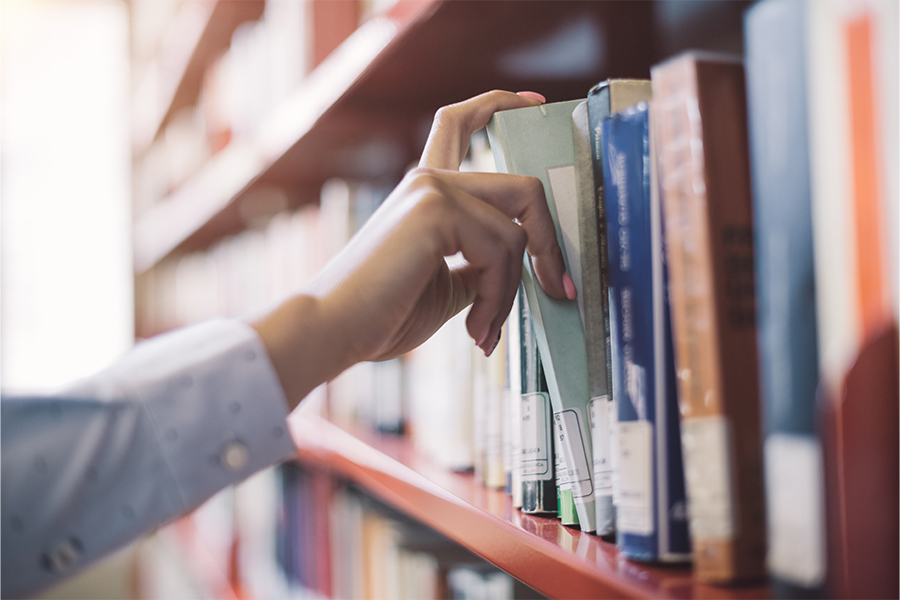 a hand grabing a folder or a book on a library shelf