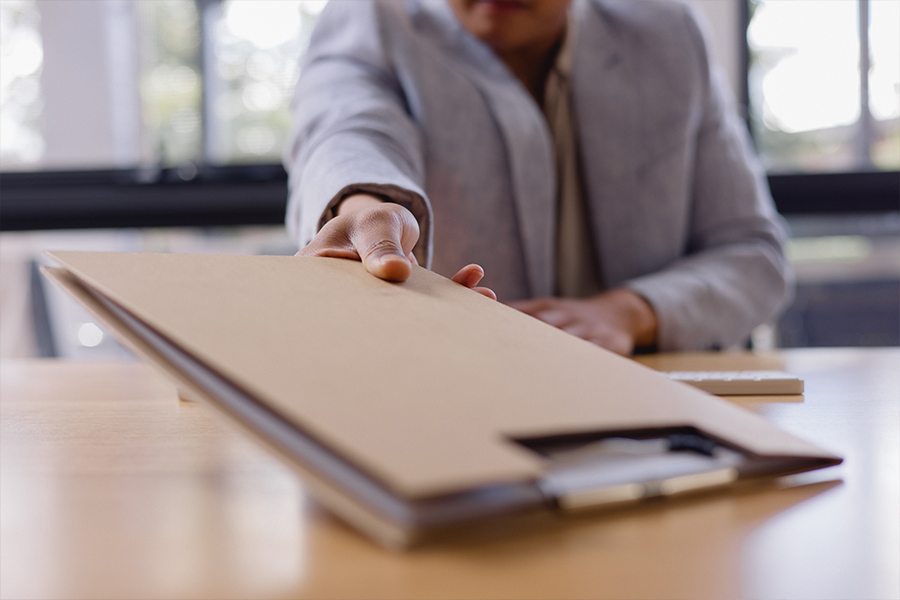 a woman handing a folder with paperwork in an office.