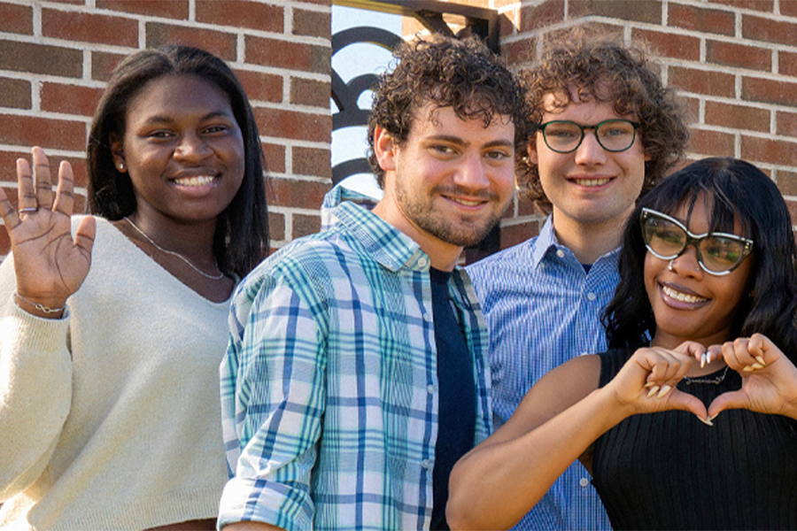Four FCC students stand together outside, smiling, with one student making a heart shape with her hands.