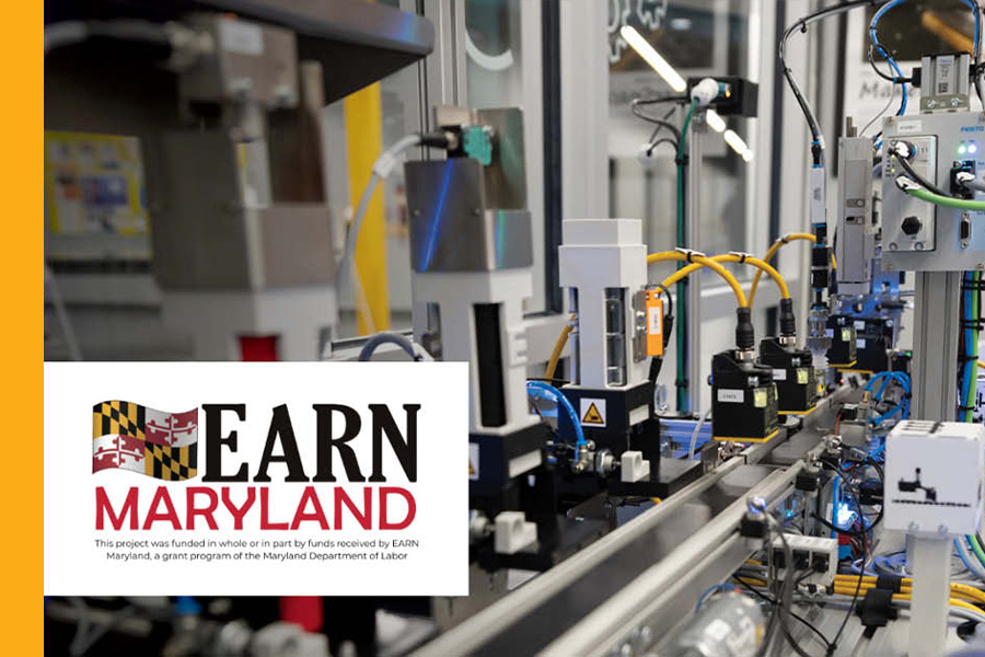 An automated industrial machine with robotic components and yellow cables, featuring the EARN Maryland logo and a funding disclaimer from the Maryland Department of Labor.