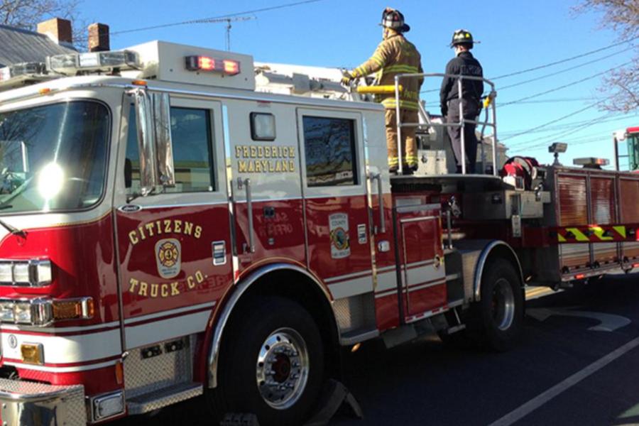 Firefighters standing on a red "Citizens Truck Co." ladder truck from Frederick, Maryland.