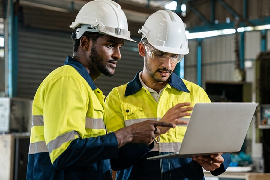 Two mechanical technicians in hard hats review information on a laptop in a warehouse