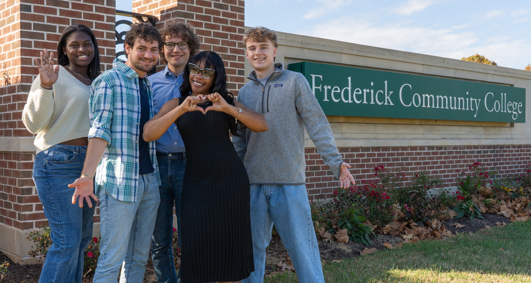 group of students in front of fcc sign make heart sign with hands